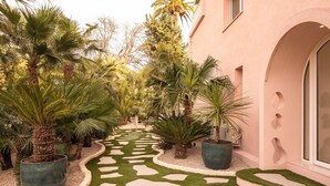 A pathway lined with palm trees and a building with an arched entrance. - Maison Carla Rosa (Cannes)