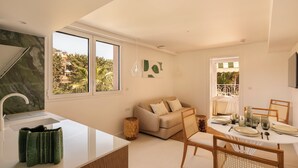 A modern kitchen with a white countertop, a sink, and a window overlooking a garden. - Maison Carla Rosa (Cannes)