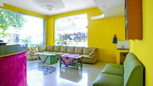 A bright yellow room with a sofa, a green sofa, a pink table, and a small table with a patterned tablecloth. - OYO 90863 Omah Kost Syariah (Tulungagung)