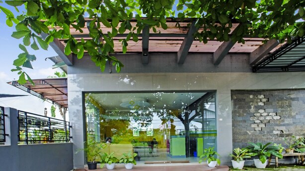 A modern building with a glass entrance, potted plants, and a brick pathway. - OYO 90863 Omah Kost Syariah (Tulungagung)