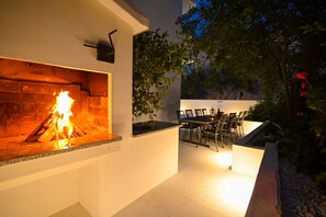 Enjoy al fresco dining or relaxation in a serene outdoor space with a fireplace and lush surroundings.