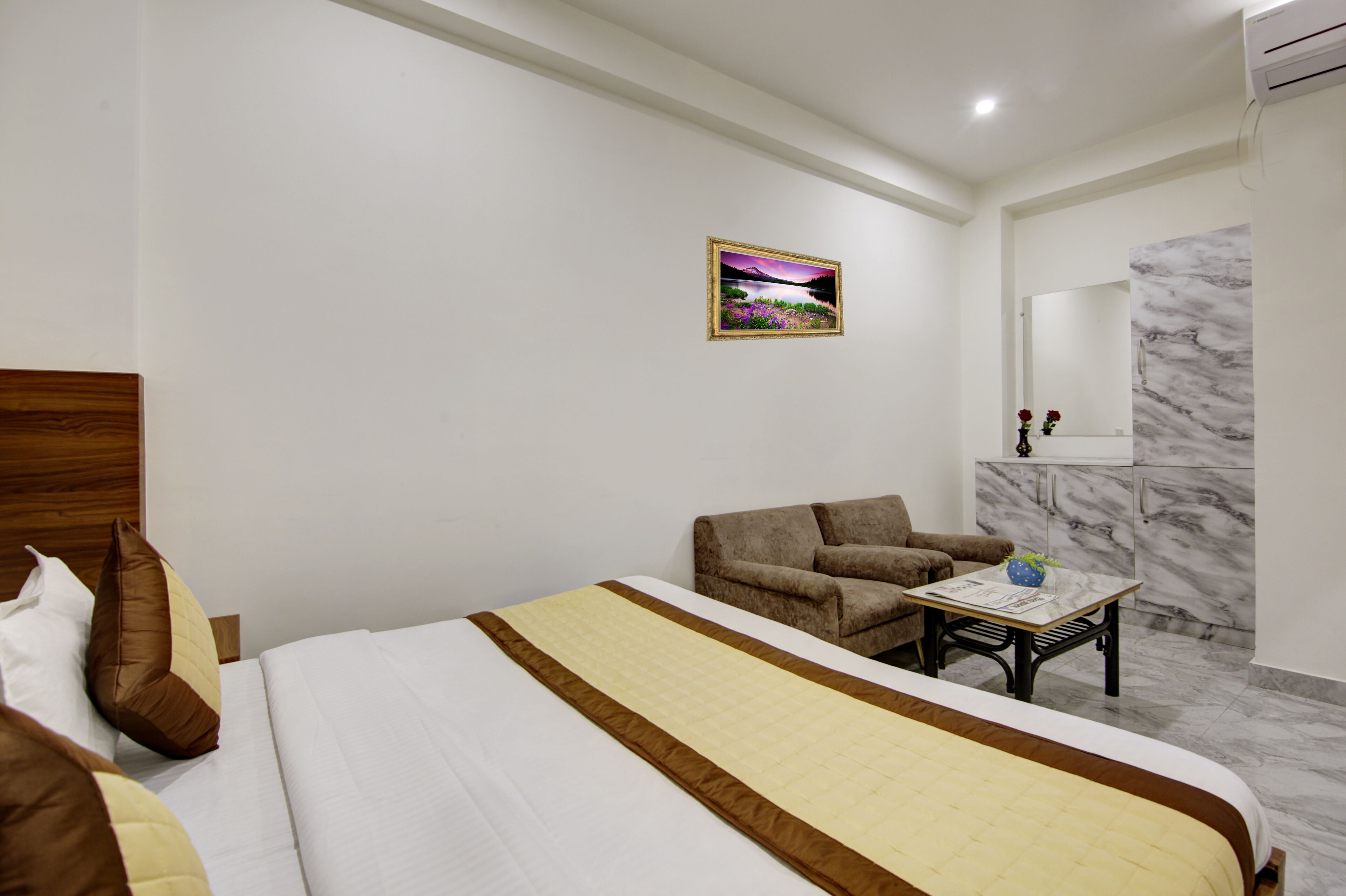 A hotel room with a bed, a sofa, a small table with a vase, and a marble wall.