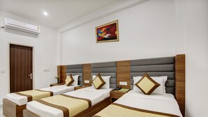 A hotel room with three beds, each with a wooden frame and a grey upholstered headboard. There is a painting on the wall above the beds. - Hotel S B Inn Paharganj (New Delhi)