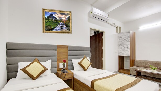 A hotel room with two beds, a sofa, a marble accent wall, and a framed picture of a waterfall. - Hotel S B Inn Paharganj (New Delhi)