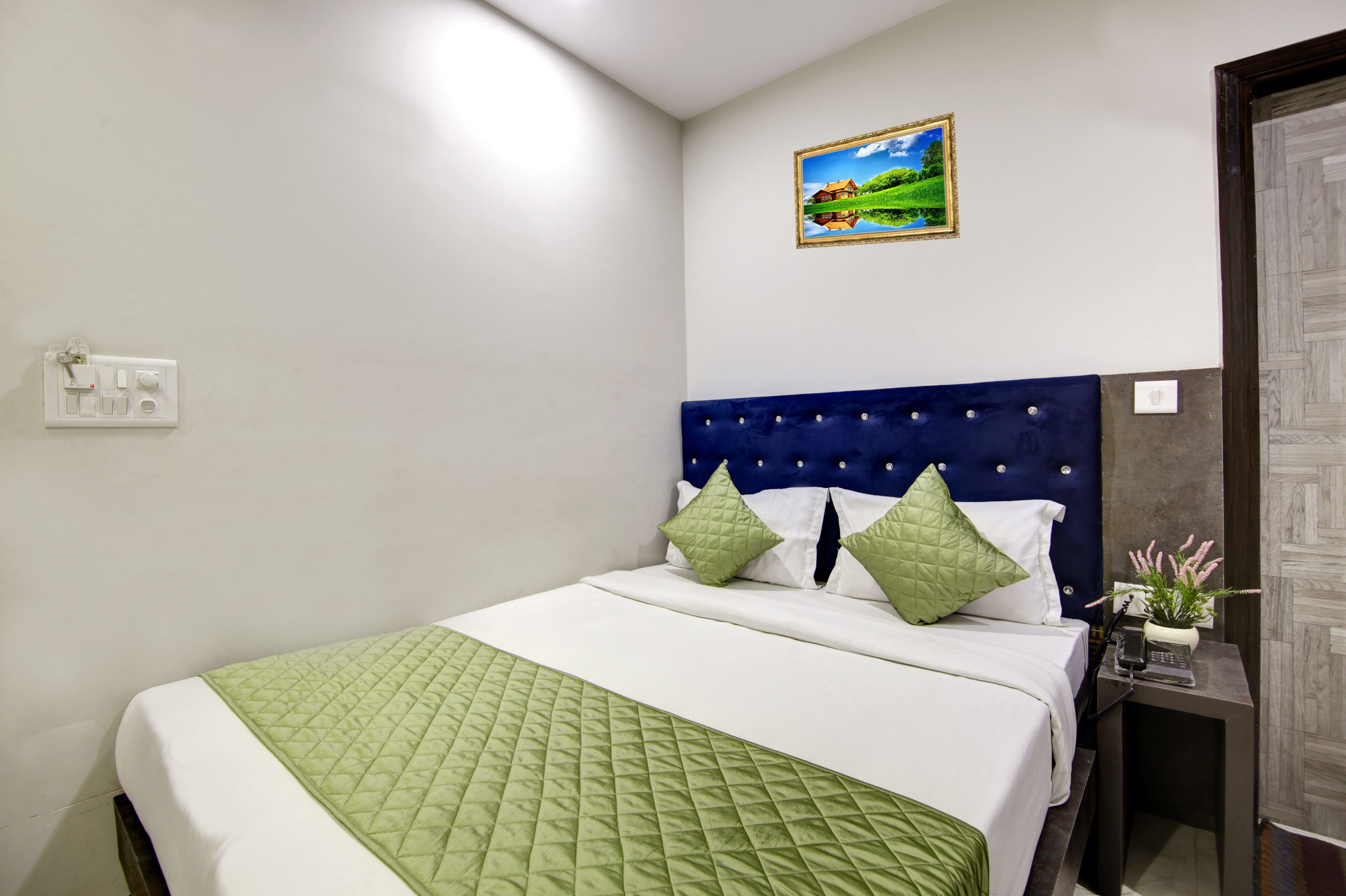 A neatly made bed with a quilted green blanket, a blue upholstered headboard, and two green pillows.