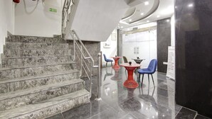 A lobby with marble stairs, red and blue chairs, a glass wall, and a fire extinguisher. - Hotel S B Inn Paharganj (New Delhi)