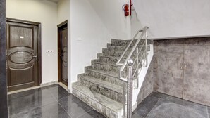 A staircase with marble steps and metal railings, leading to a landing with a fire extinguisher mounted on the wall. - Hotel S B Inn Paharganj (New Delhi)