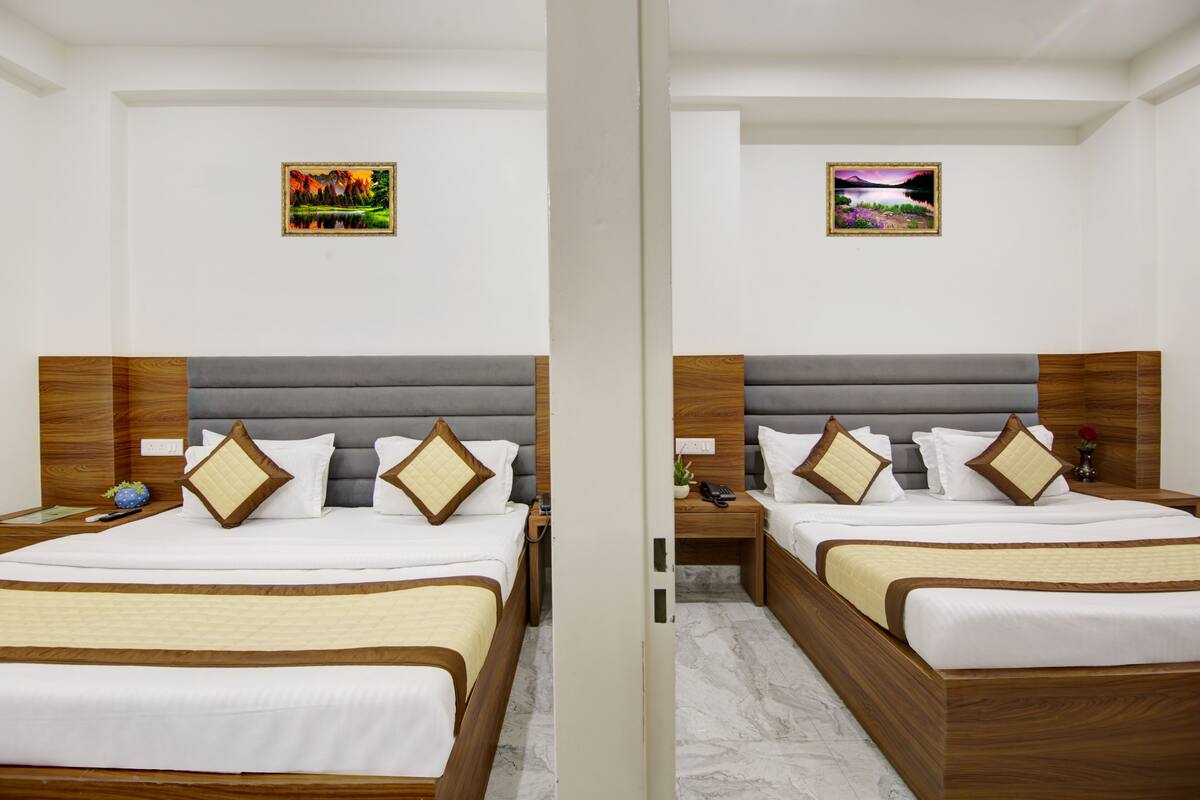 A hotel room with two beds, wooden headboards, white bedding, and two framed pictures on the walls.