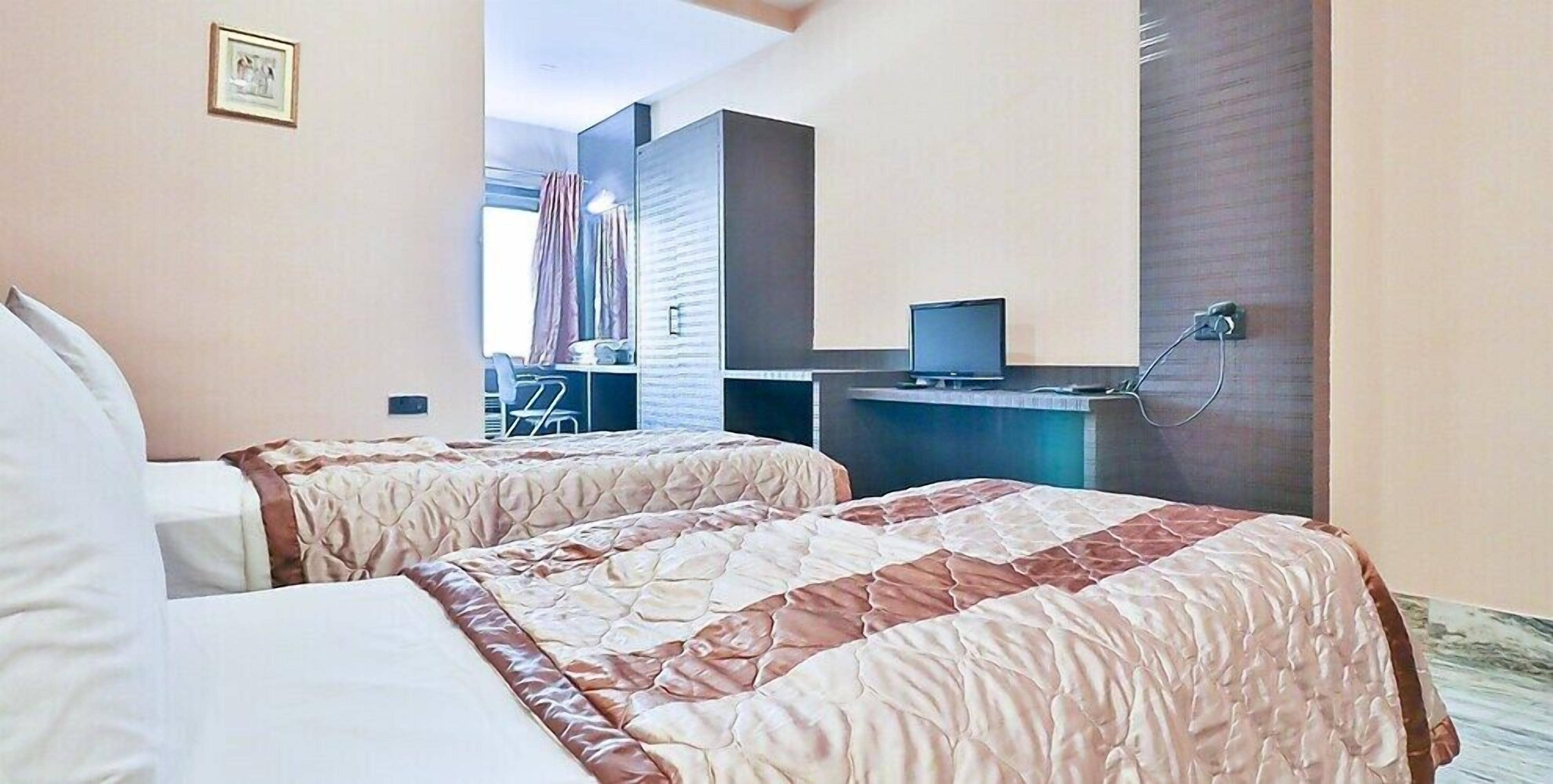 A hotel room with two beds, a desk with a computer, and a shower area.