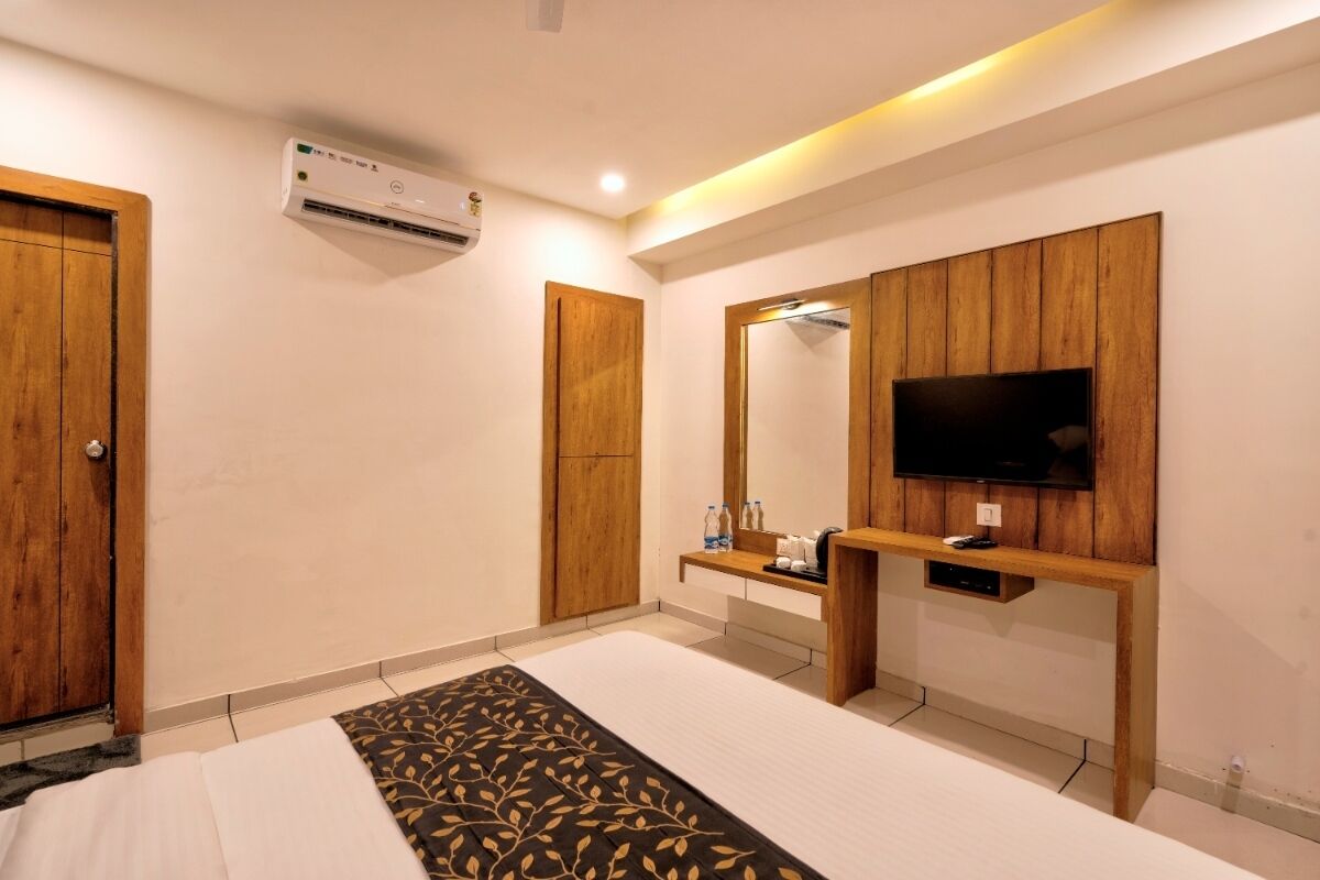 Una habitación de hotel con cama, televisión, espejo, armario de madera y aire acondicionado.