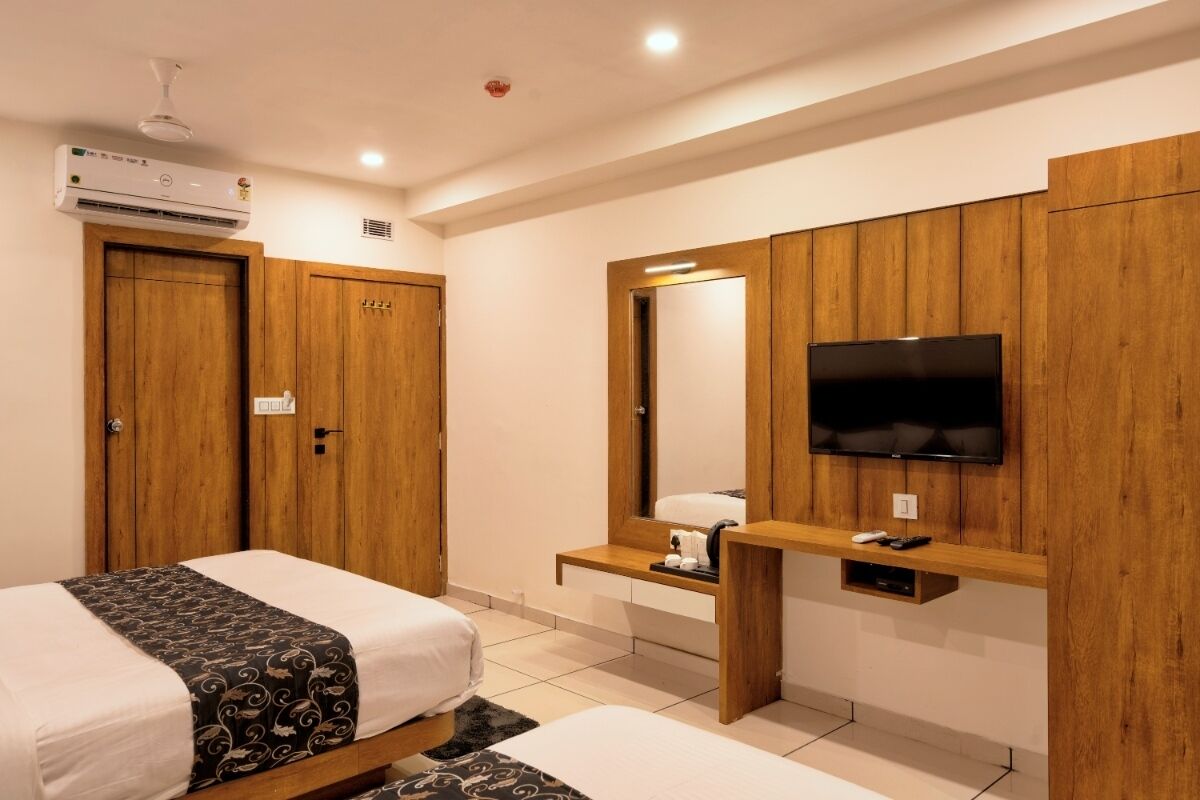 Een hotelkamer met twee bedden, een televisie bevestigd aan een houten paneelwand, een spiegel en een airconditioner.