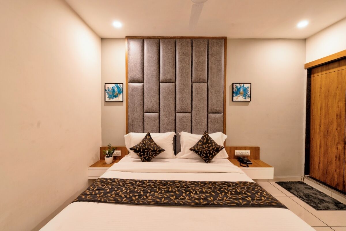 A modern hotel room with a large bed, a wooden headboard, two bedside tables with lamps, and a wooden wardrobe.