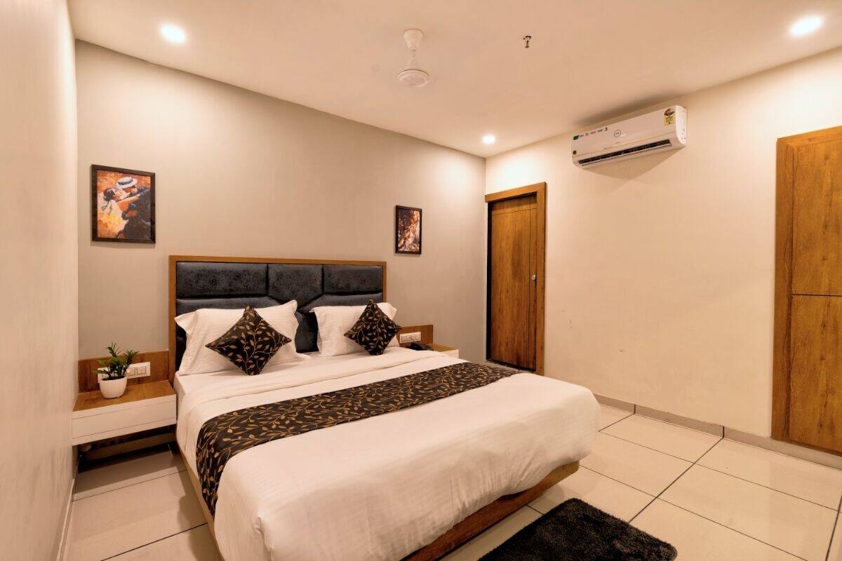 Une chambre à coucher bien aménagée, avec un grand lit, des tables de chevet, un climatiseur fixé au mur et une porte.