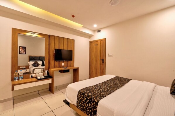 A hotel room with a bed, a TV mounted on the wall, a wooden wardrobe, a bedside table with a lamp, and a mirror.