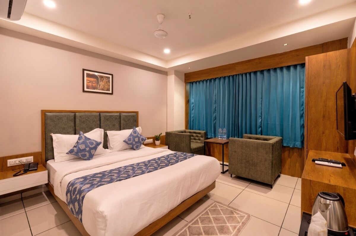 A hotel room with a large bed, a desk, a chair, a TV, and a window with curtains.