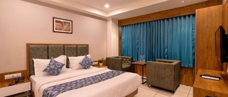 A hotel room with a large bed, a desk, a chair, a TV, and a window with curtains.