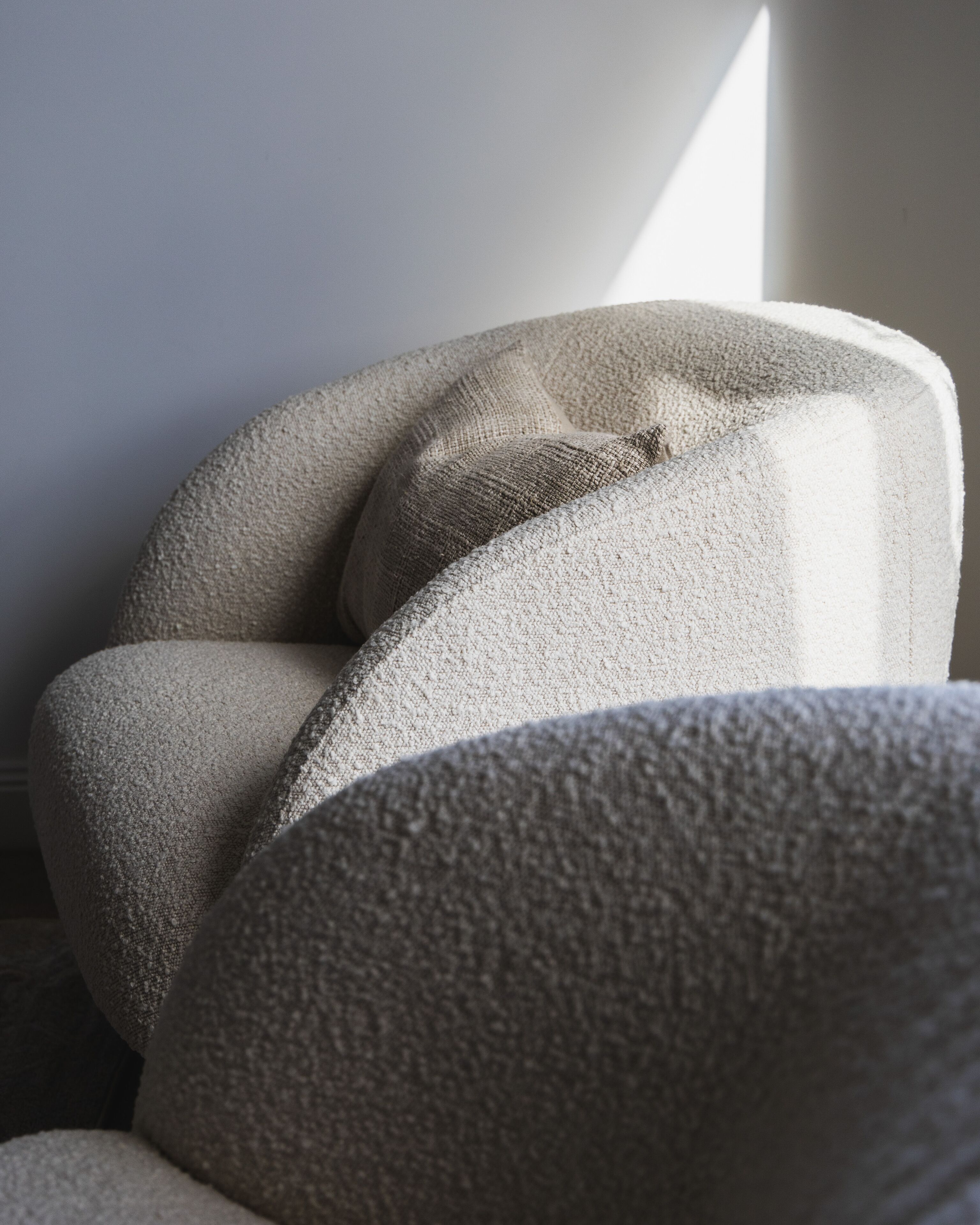 Een detailfoto van een gestoffeerde stoel met een gladde, afgeronde rugleuning en armleuningen.