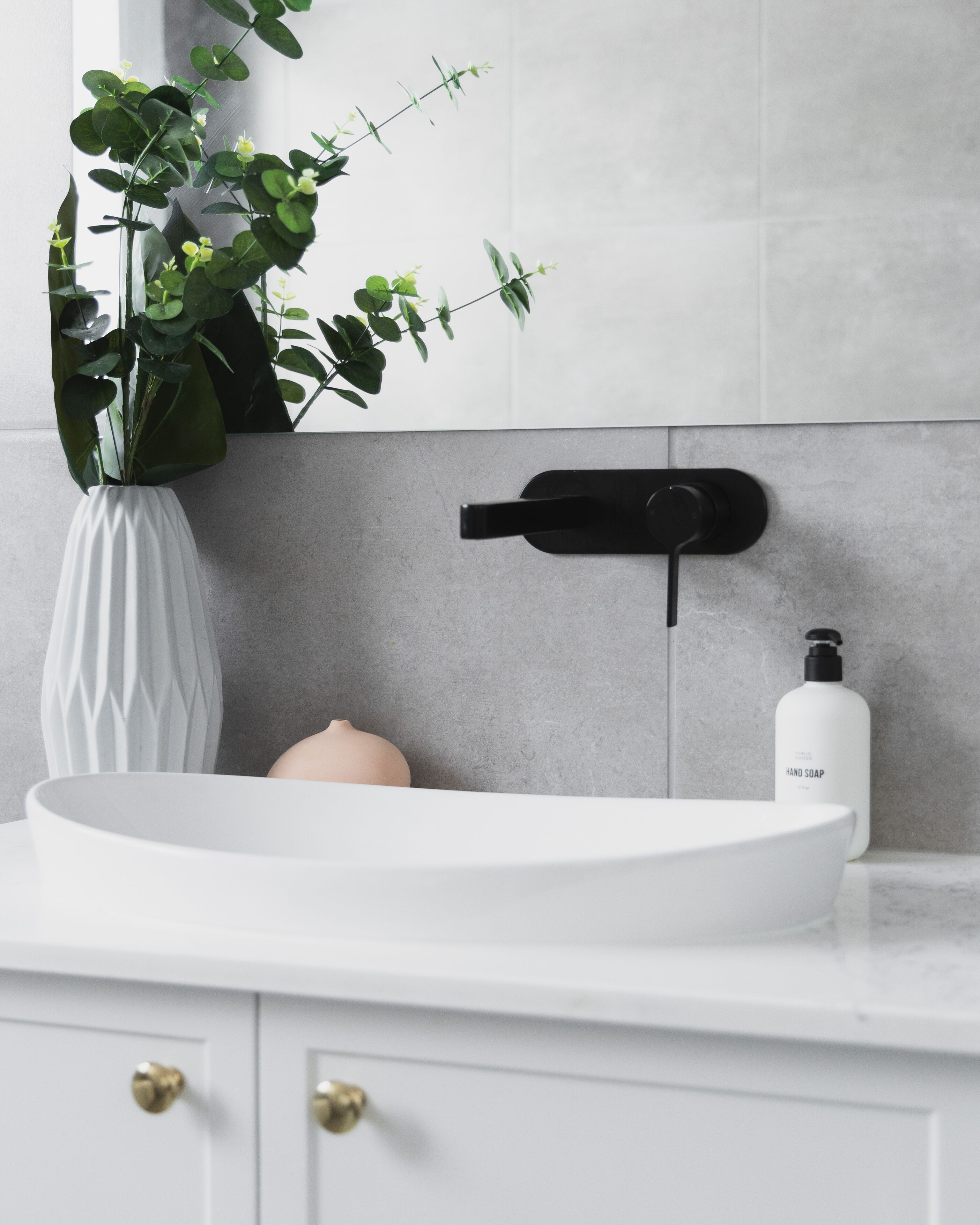 A modern bathroom with a white sink, a potted plant, a soap dispenser, and a black faucet.