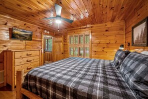 A wooden cabin bedroom with a bed, dresser, and a ceiling fan.