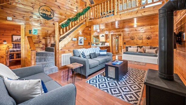 A log cabin interior with a staircase, a living room with a sofa and coffee table, and a fireplace. - Peaceful 3BR GBurg w/Hot Tub + Fireplace* Privacy! (Sevierville)