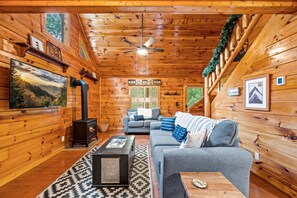 A cozy cabin interior with a fireplace, a sofa, a coffee table, and a ceiling fan.