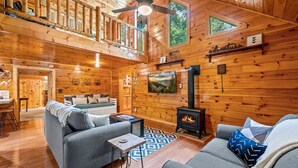 A cozy cabin interior with a fireplace, wooden walls, a sofa, and a dining area. - Peaceful 3BR GBurg w/Hot Tub + Fireplace* Privacy! (Sevierville)