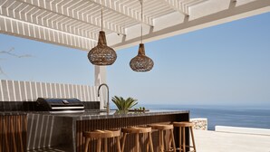Een openluchtcafé met uitzicht op de oceaan, met een modern ontwerp, een betonnen aanrecht, houten krukken en hangende rieten lampen.