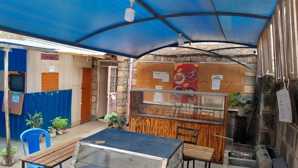 A small outdoor seating area with a table and chairs, a popcorn stand, and a reception sign. - Savannah Road (Nairobi)