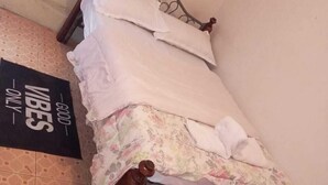 A small, single-bed room with a metal frame, a floral bedspread, and a sign on the wall. - Savannah Road (Nairobi)