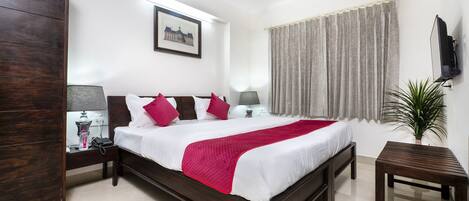 A neatly arranged bedroom with a large bed, a bedside table with a lamp, a small table, and a potted plant.