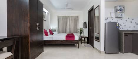Une chambre d’hôtel comprenant un lit, un bureau, une armoire, un ventilateur de plafond, une télévision et un coin cuisine avec un réfrigérateur et un évier.