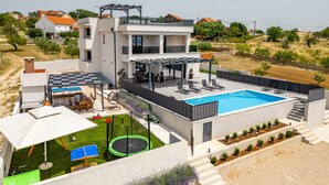 Een modern huis met twee verdiepingen, een zwembad, terras en een trampoline.
