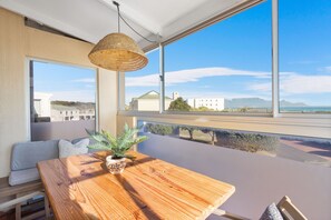 A room with a large window, a wooden table, a woven light fixture, and a potted plant.