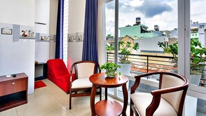 Een moderne woonkamer met een rode bank, twee fauteuils, een kleine houten tafel met een plant en uitzicht op de stadsgezicht door grote ramen.