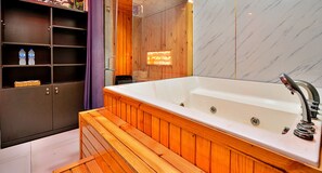 Une salle de bain moderne avec un banc en bois, une grande baignoire et une étagère contenant des bouteilles d’eau.