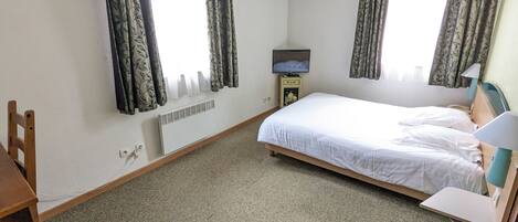 Une chambre à coucher avec un lit, un bureau, une chaise, un téléviseur et un radiateur.