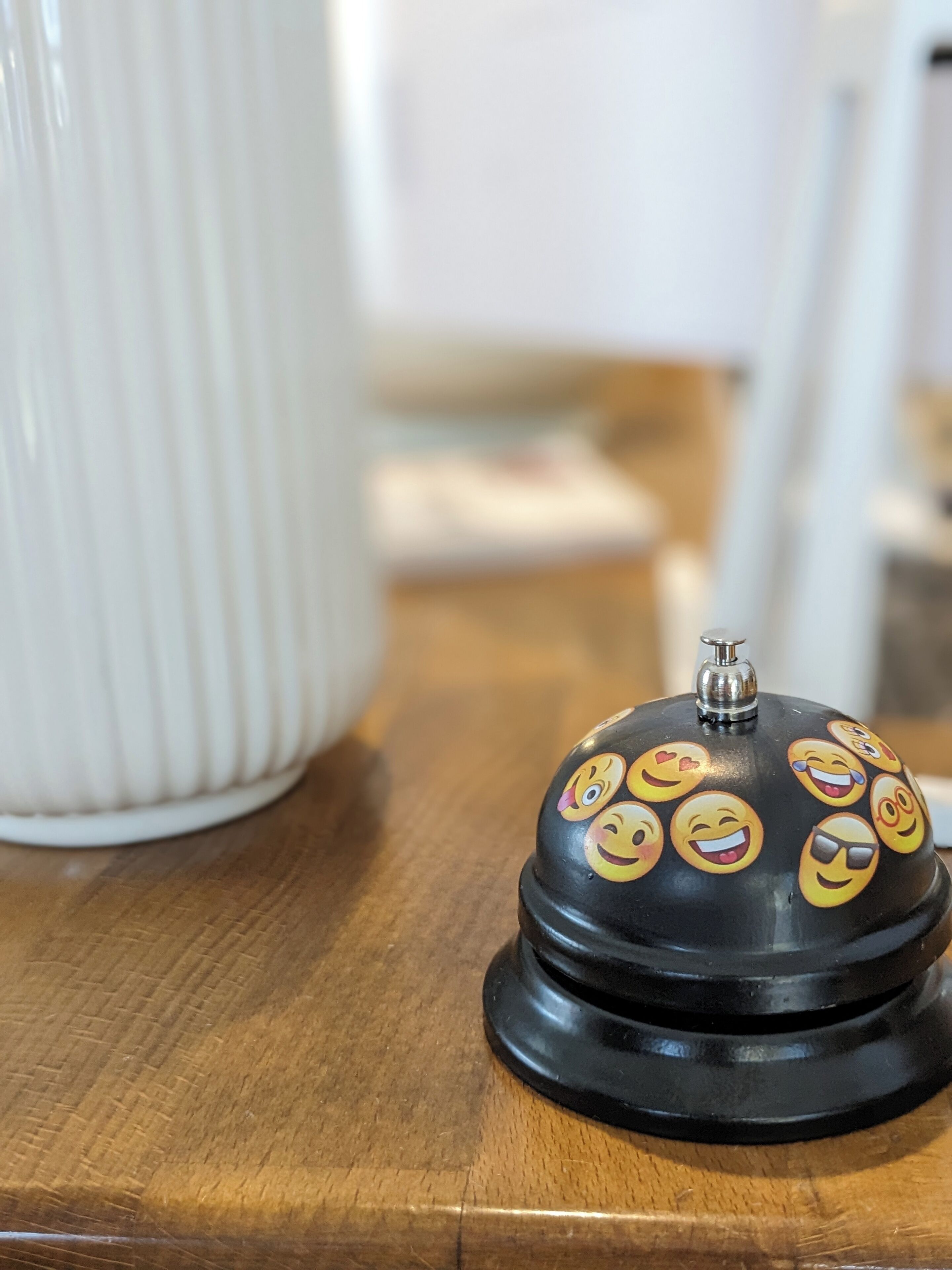 A black bell with a metallic top, adorned with various emoji faces, placed on a wooden surface.