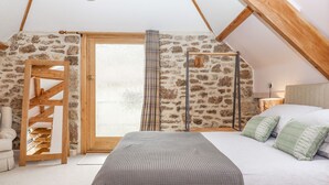 A bedroom with a stone wall, wooden beams, a bed with green pillows, and a wooden wardrobe. - The Coach House at Thorn Farm (Exeter)