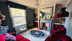 Een woonkamer met rode banken, een open haard, een kroonluchter en een groot raam.