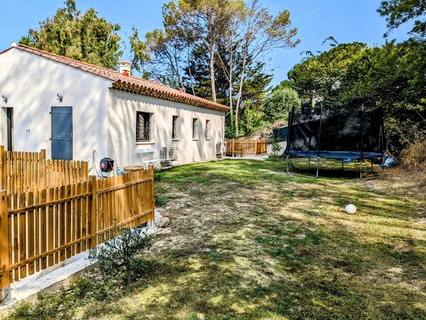 Una casa con fachada blanca y techo de tejas rojas, rodeada por una cerca de madera y un jardín con césped.
