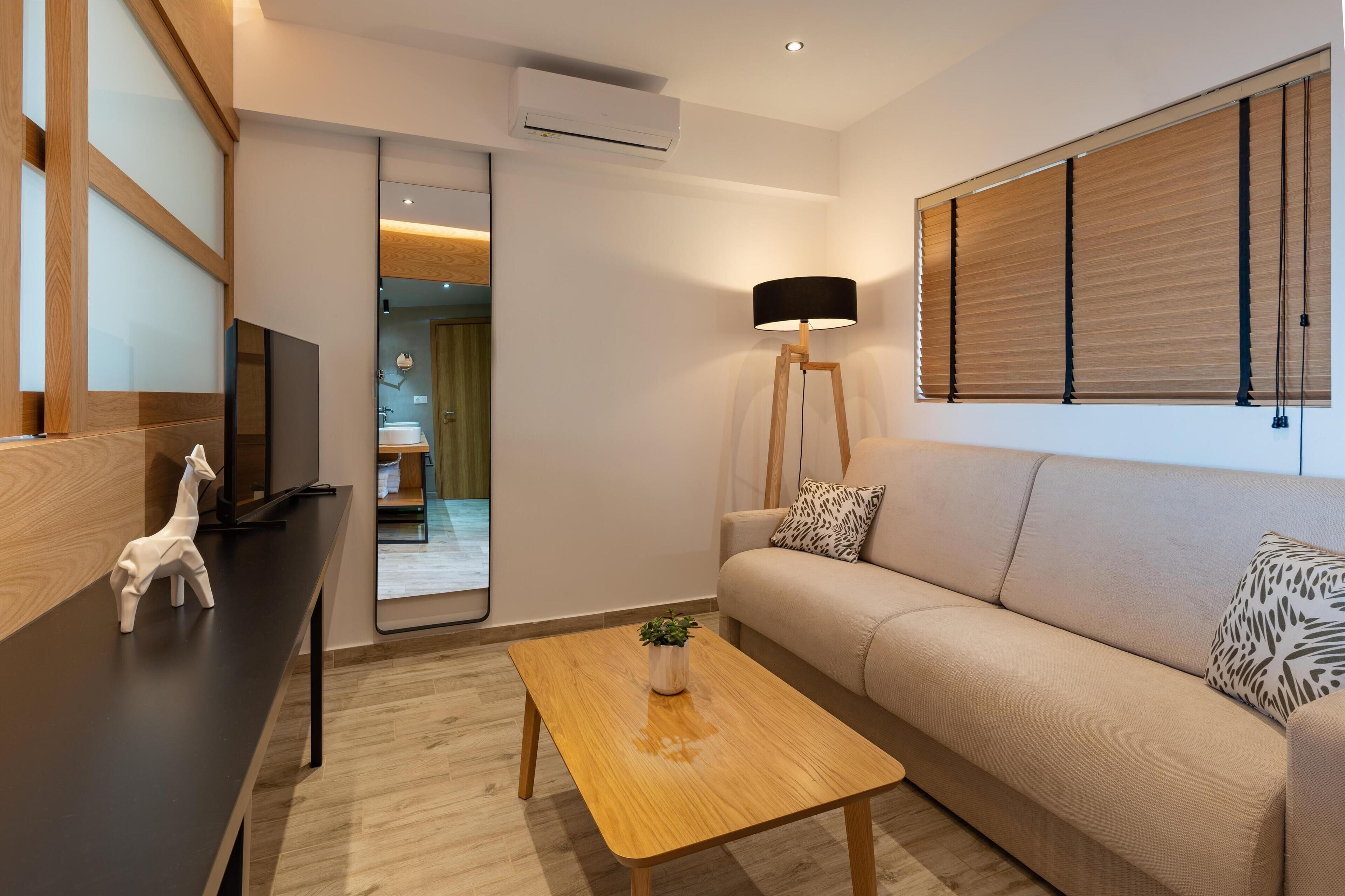 Una sala de estar moderna con un sofá, una mesa de centro con una planta, una lámpara y un televisor sobre un mueble de madera.