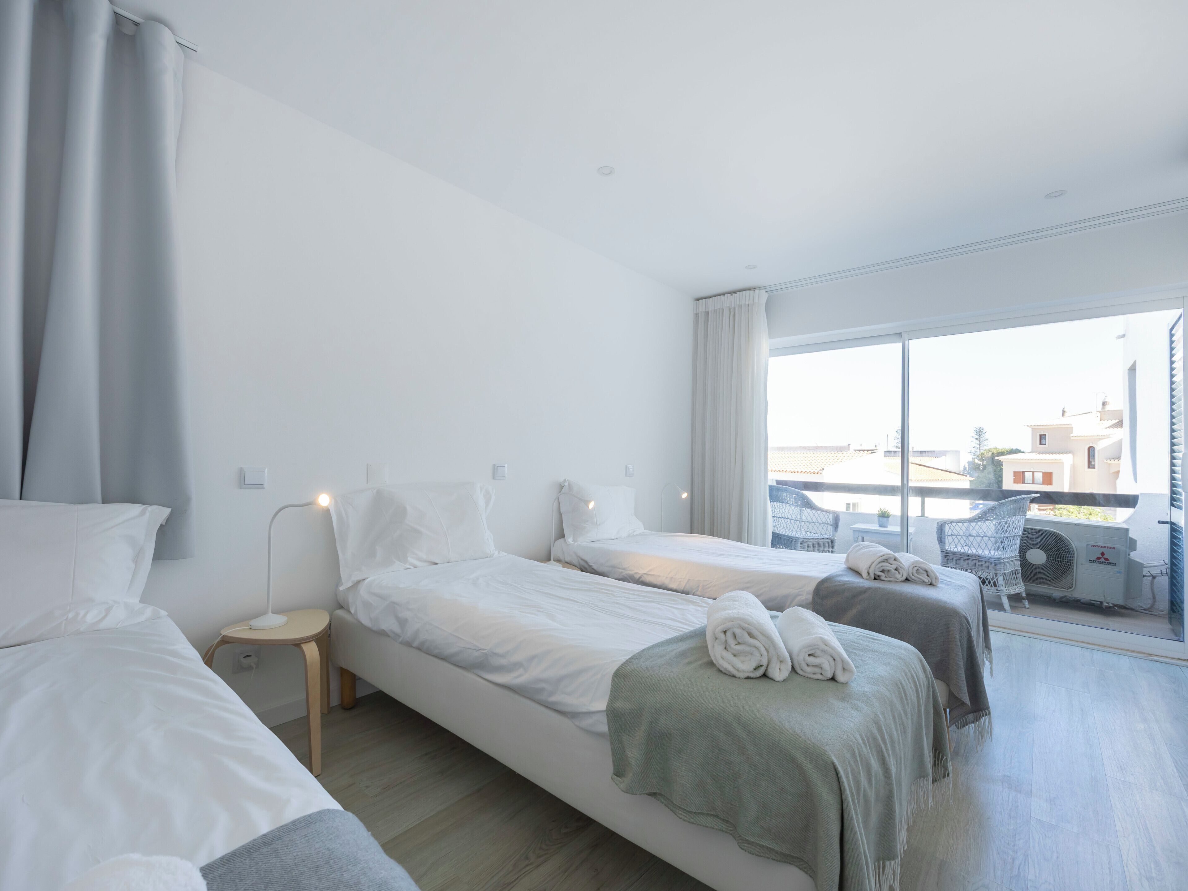 Ein Hotelzimmer mit zwei Betten, einem kleinen Tisch, einem Stuhl und einem großen Fenster mit Blick auf Gebäude.