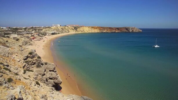 Eine Küstenlandschaft mit Sandstrand, felsigen Klippen und blauem Meer.