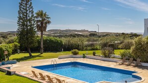 Ein rechteckiger Pool mit integrierter Leiter, umgeben von einer gepflasterten Liegefläche. Sonnenliegen sind rund um den Pool aufgestellt.