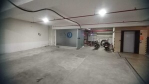 A parking garage with concrete floors and walls, a blue sign with the number 9, and a motorcycle parked near an elevator. - Pondy Heights - Suites and Studios (Puducherry)