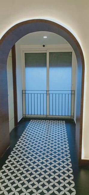 Un couloir au sol décoré de motifs menant à un balcon doté d’une rambarde en métal.