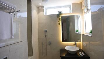 Un baño moderno con cabina de ducha de vidrio, un lavabo blanco y un espejo con un ventanal encima.