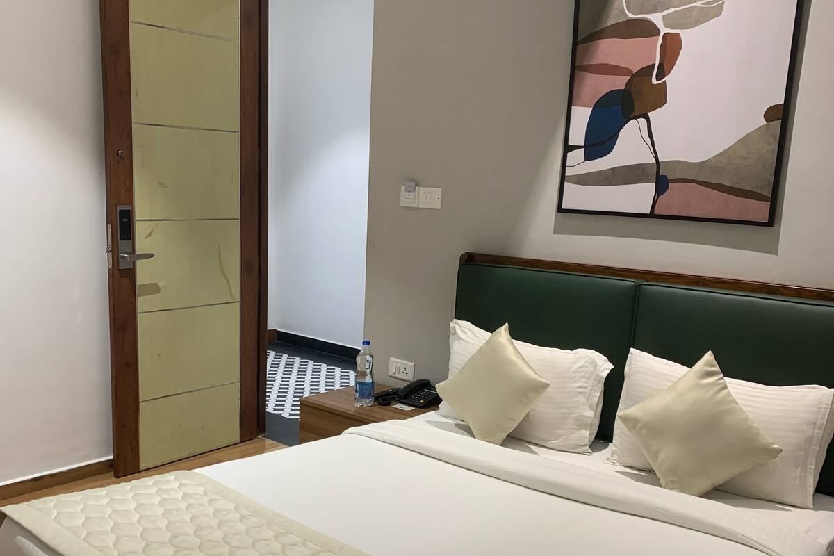 A hotel room with a bed, a nightstand, a wall-mounted painting, and a door.