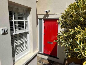 Stylish entrance with a red door, white shutters, and a potted plant.