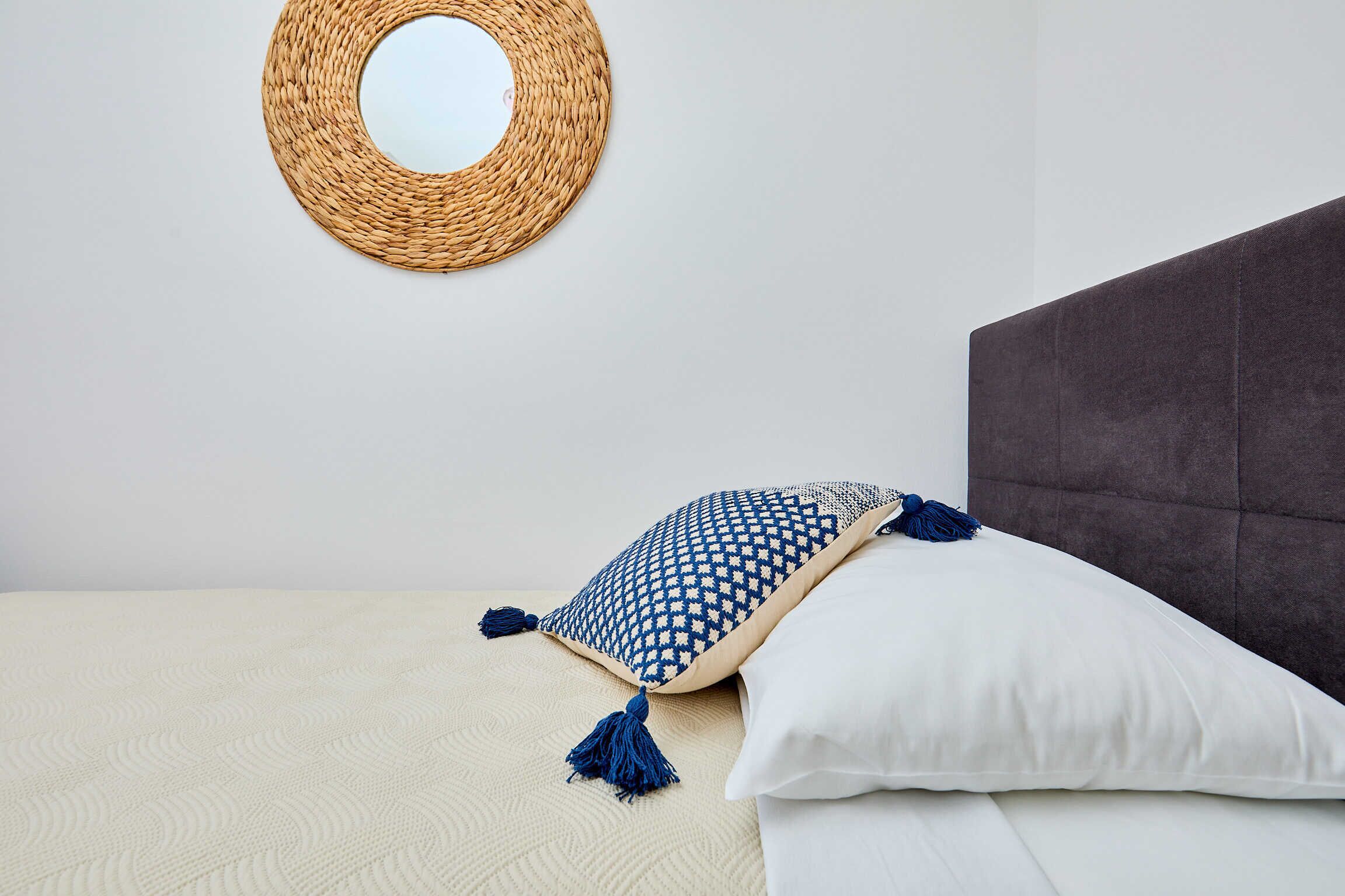 Un lit bien fait, avec un oreiller à motifs blancs et bleus, un oreiller blanc uni et une tapisserie murale tissée au-dessus.